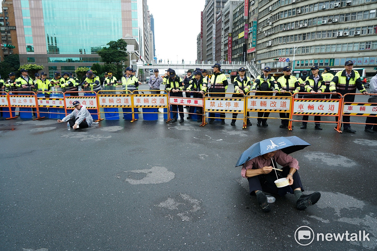 一場小雨加上正逢中午用餐時間，大部分的抗議的退役軍人紛紛離開陳抗現場吃飯或躲雨，但，仍有幾位退役軍人仍堅持不離開現場，在警方的人牆前撐著傘席地而坐，在雨中吃便當，表現了不怕苦、不怕難的軍人本色。 圖：張良一/攝