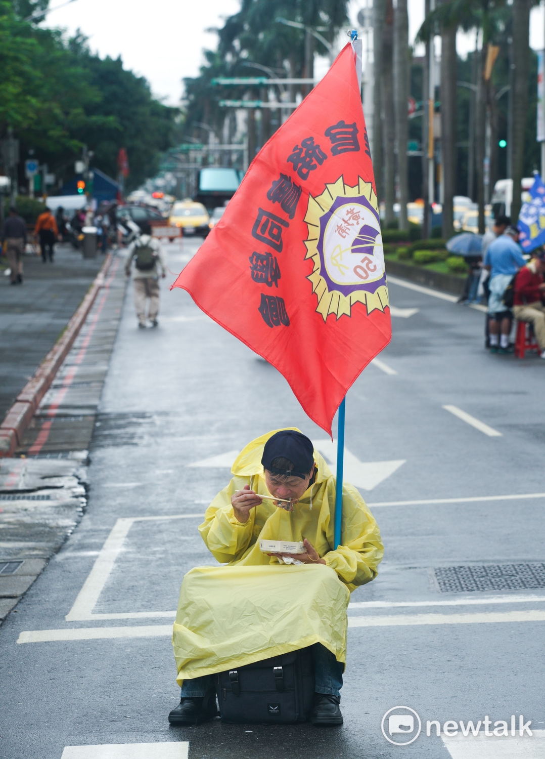 一位拿著『陸官務實同學會』旗幟的退役軍人，堅持抗爭到底的精神，堅守陳抗崗位，他穿著雨衣，在封閉的中山南路上吃排骨便當。 圖：張良一/攝