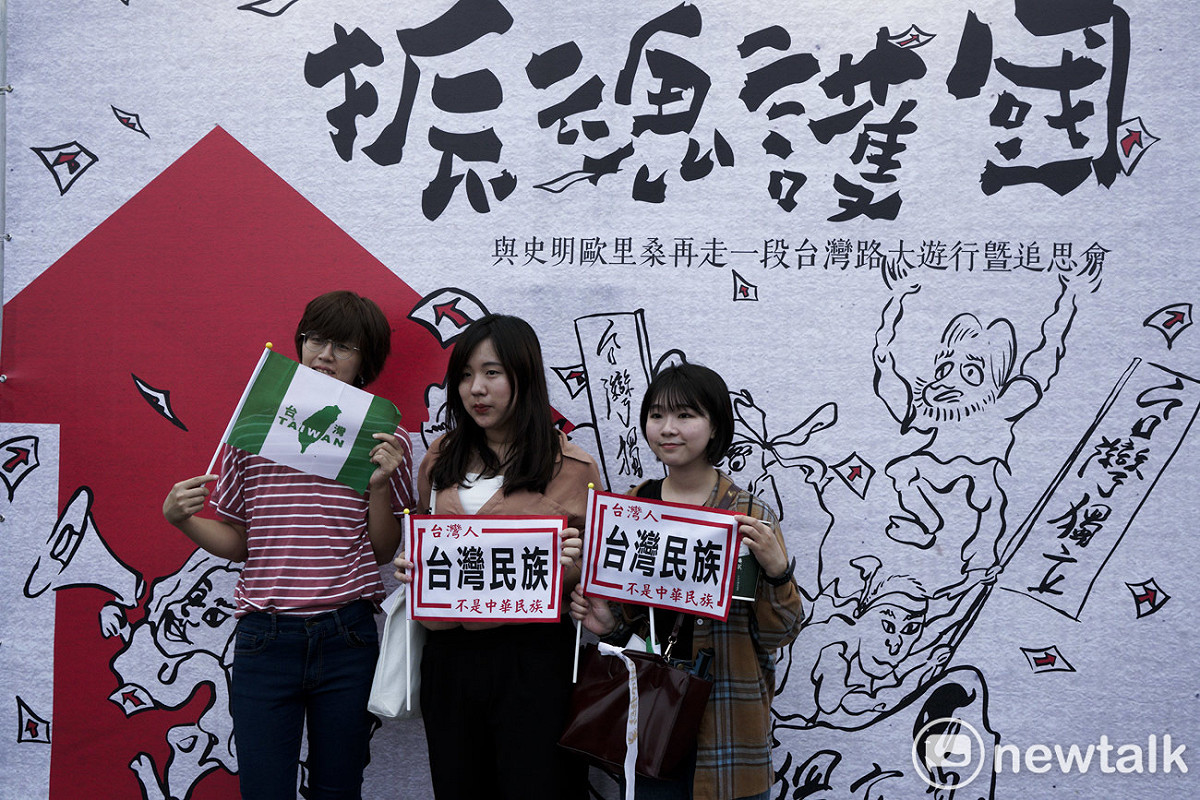三位民眾拿著『台灣民族不是中華民族』的旗子在史明追思會看板前合影。 圖：張良一/攝