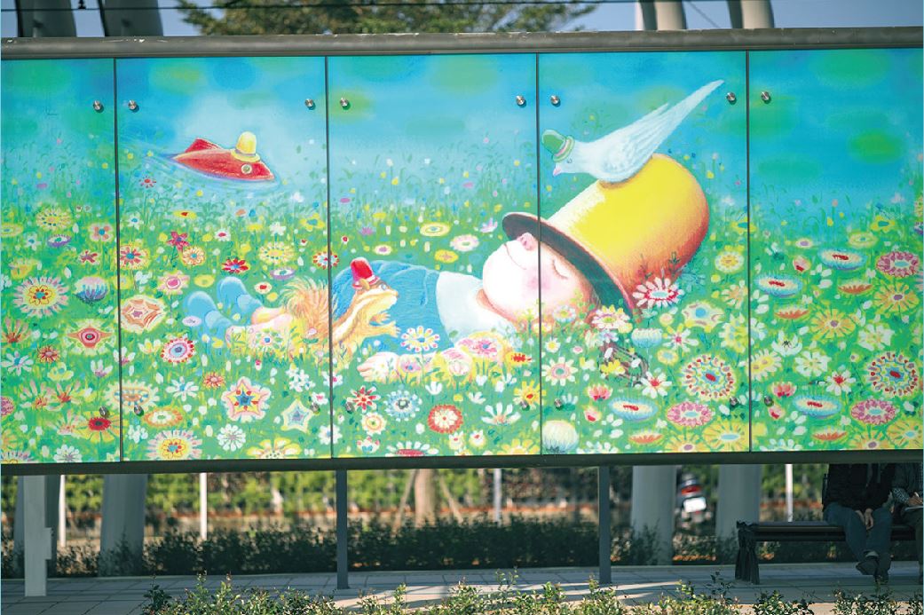 崁頂站有一大片彩繪玻璃牆，孩子躺在花叢裡等待下一次旅途展開。 圖：翻攝自淡海輕軌導覽手冊