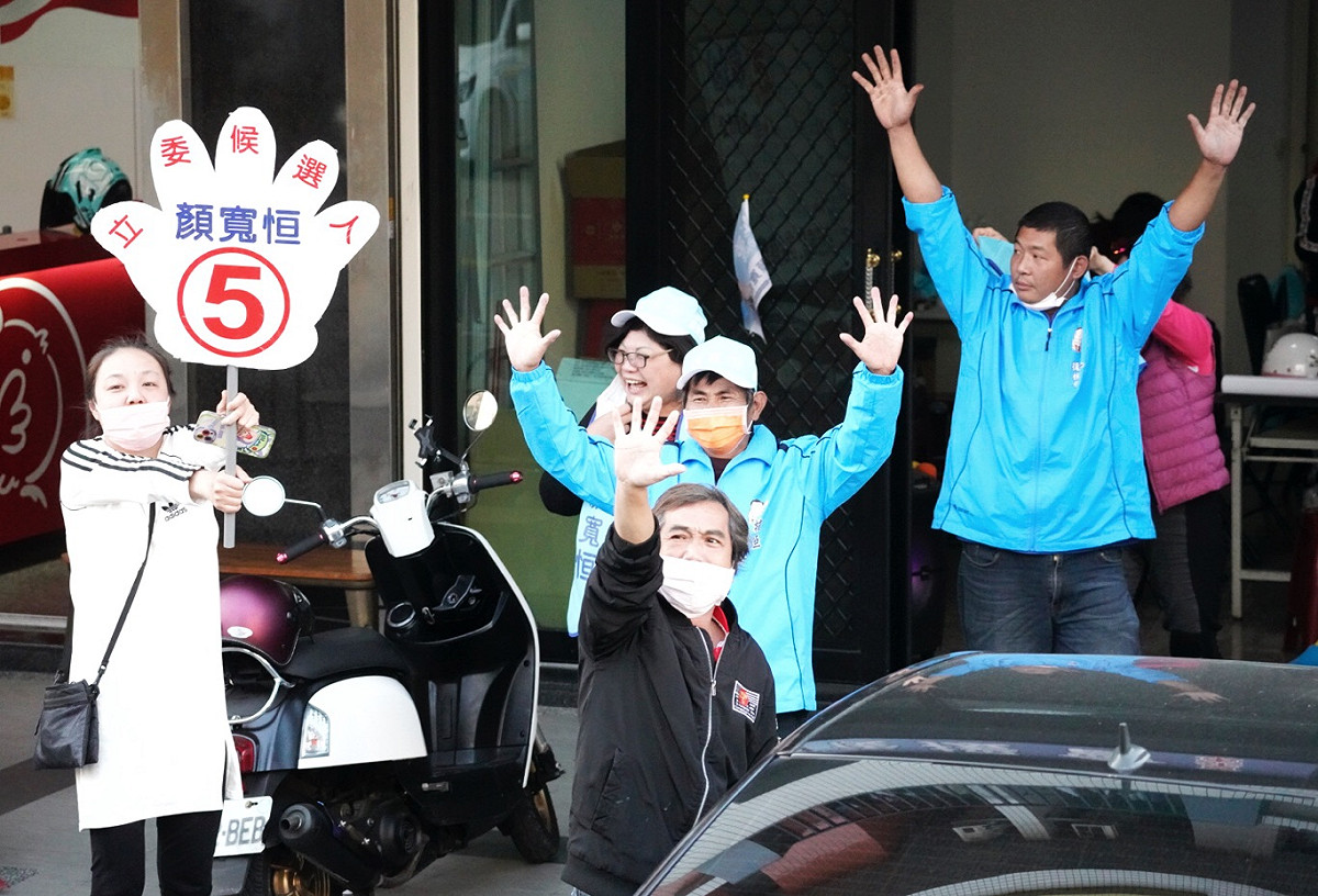 民進黨台中二選區立委補選候選人林靜儀下午在霧峰市區掃街時經過顏寬恒的服務處，其工作人員對著林靜儀的掃街車隊比出5號手勢。 圖：張良一/攝