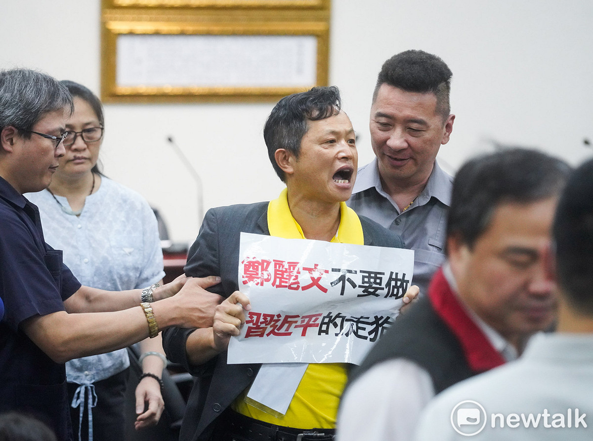 台灣國理事長陳峻涵在國民黨主席鄭麗文舉行訪美返國記者會前，手持「鄭麗文不要做習近平的走狗」牌子，並高喊抗議口號。 圖：張良一/攝