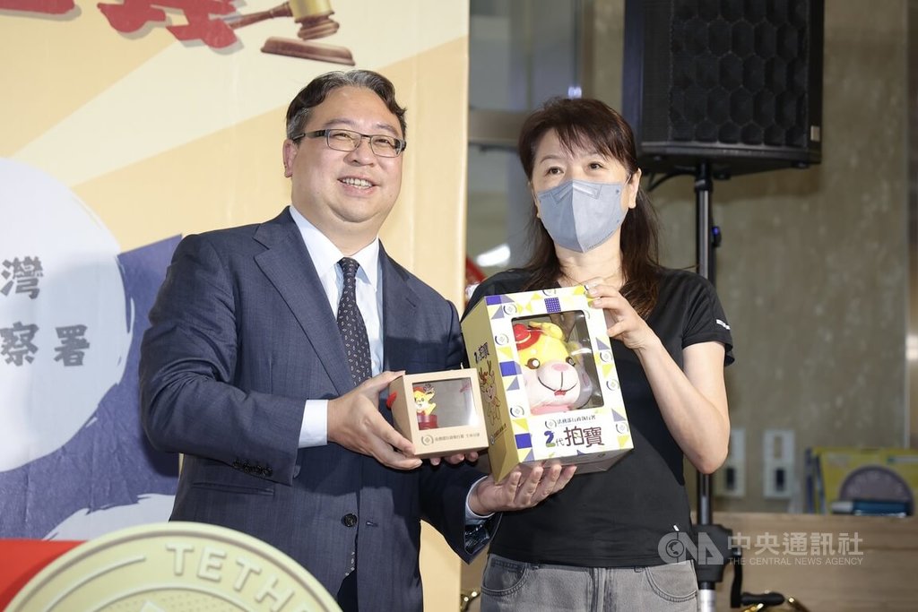 法務部行政執行署11日上午舉辦「檢執聯防 守護正義」拍賣活動，因應雙11購物節，法務部政務次長黃世杰（左）贈禮給首位得標泰達幣的民眾。中央社記者翁睿坤攝　114年11月11日