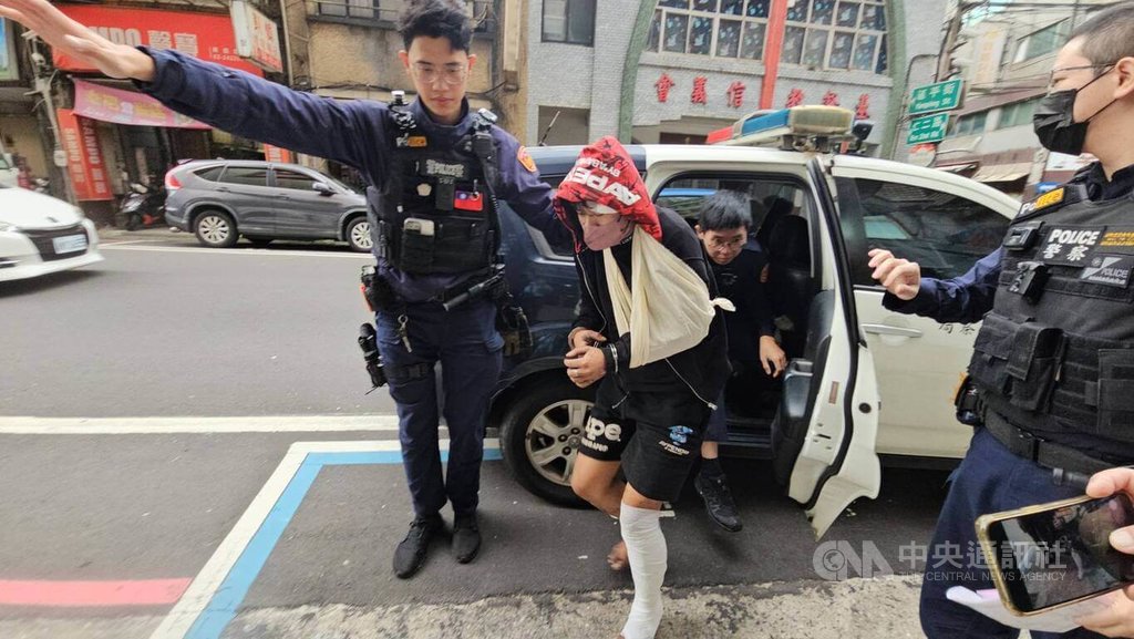 通緝犯黃姓男子（左2）26日凌晨開車拒檢，衝入基隆市一處平交道，飆駛鐵軌不久後爆胎，黃男棄車逃逸，疑攀爬鋼梁至基隆火車站頂樓，墜落3樓雨棚，經送醫治療後無大礙，員警將黃男帶回警局詢問。中央社記者王朝鈺攝　114年11月26日