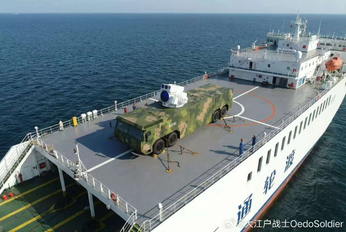 畫面中可見迷彩覆蓋的載具以粗重鐵鍊固定於船面，上方則設置大型光電砲塔，內部即為雷射發射裝置。 圖：翻攝自 微博