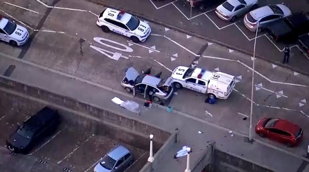 邦代海灘的槍擊現場附近，警車旁有被覆蓋的遺體和血跡。（NINE NETWORK/SEVEN NETWORK/AUSTRALIAN BROADCASTING CORPORATION/Handout via REUTERS）