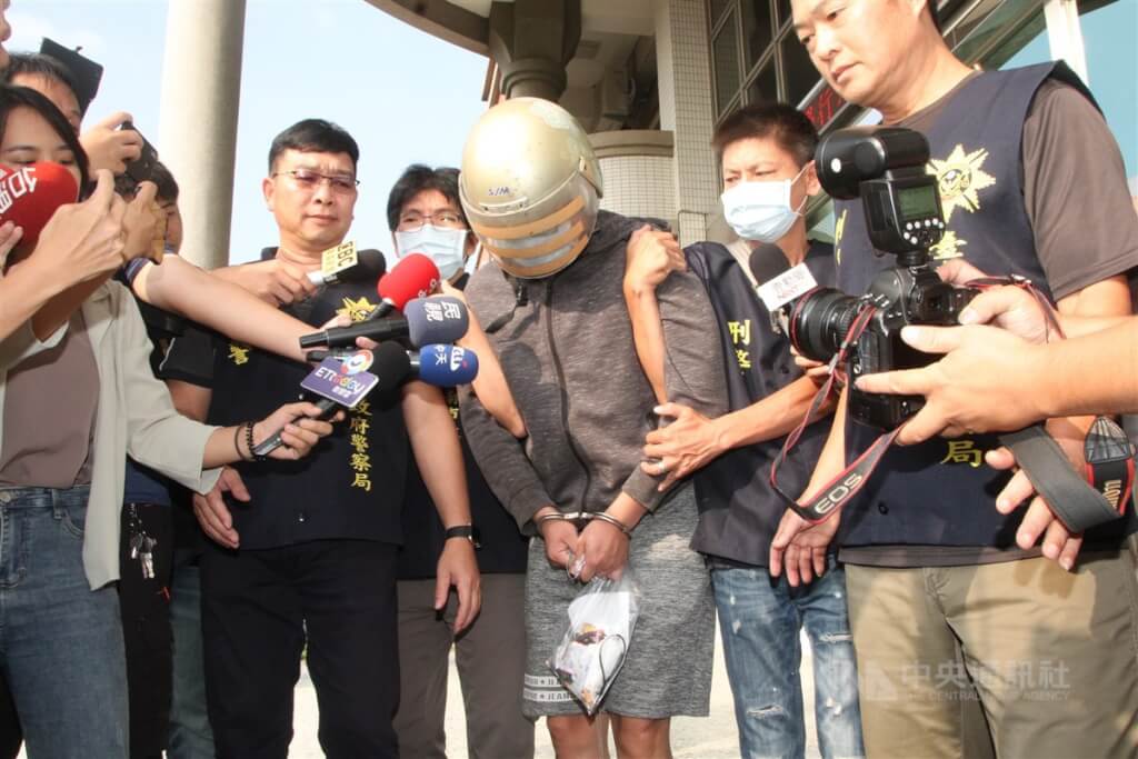 圖為2020年10月梁育誌（中）訊後被警方帶出警局移送地檢署，面對大批媒體詢問，梁育誌低頭不發一語。（中央社檔案照片）