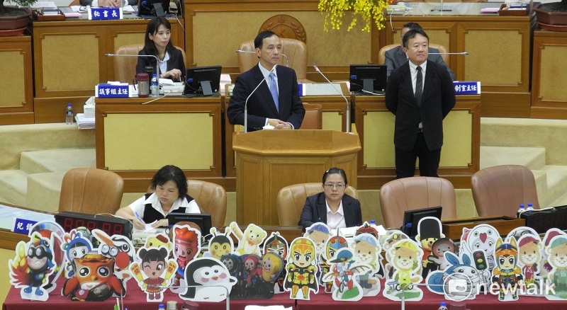 民進黨新北市議會黨團質詢市長朱立倫，擺出約40隻各局處吉祥物立牌，還調侃不如統一用民政局長江俊霆（立者右一）的「大頭」當吉祥物。 圖：王峻昌/攝