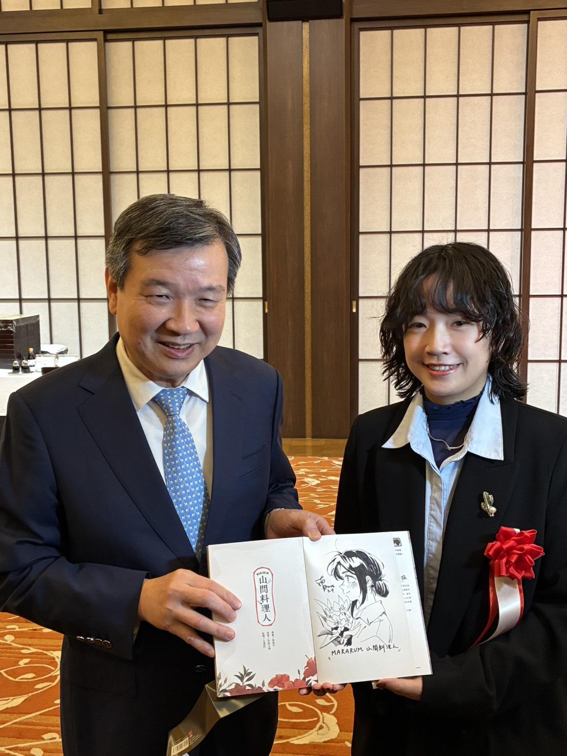 台灣漫畫家南南日致贈得獎作品《Mararum：山間料理人》予駐日大使李逸洋，並於扉頁親筆繪上主角「巴奈」畫像留念。 圖：台灣文化中心提供
