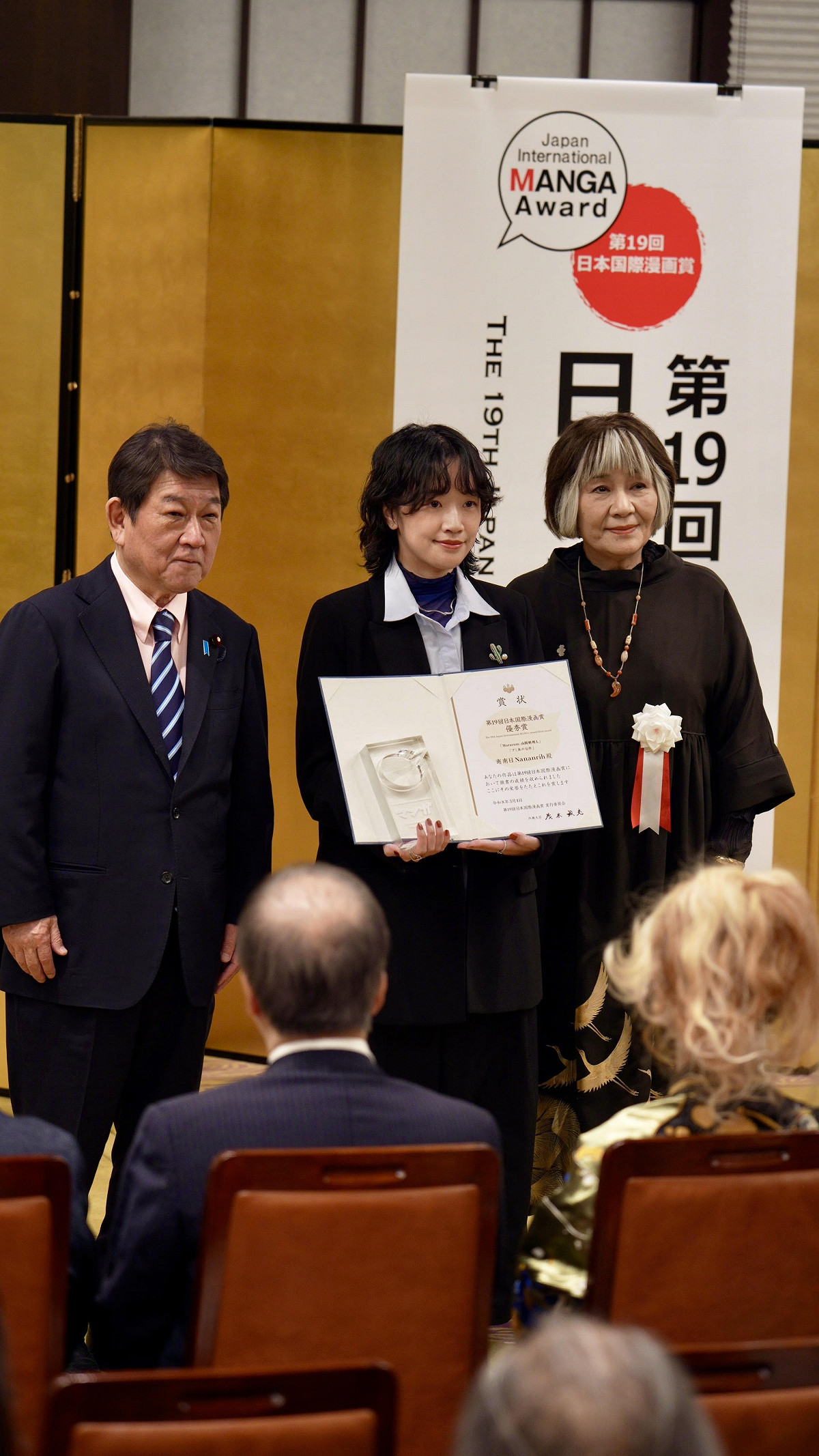 台灣漫畫家南南日（中）手持獎狀與日本外務大臣茂木敏充（左）、評審長里中滿智子（右）合影 圖：台灣文化中心提供