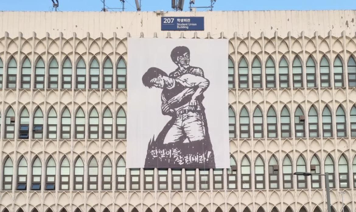 延世大學總學生會10日在該校總學生會館發表「時局宣言」，表達對選票短缺事件的不滿。現場會館後方懸掛著「讓李韓烈活過來」的布條。李韓烈為延世大學學生，1987年6月9日，他在該校正門參與示威時，遭警方發射的催淚彈擊中，最終成為韓國六月民主抗爭進一步激化的重要導火線之一。 圖：翻攝IG