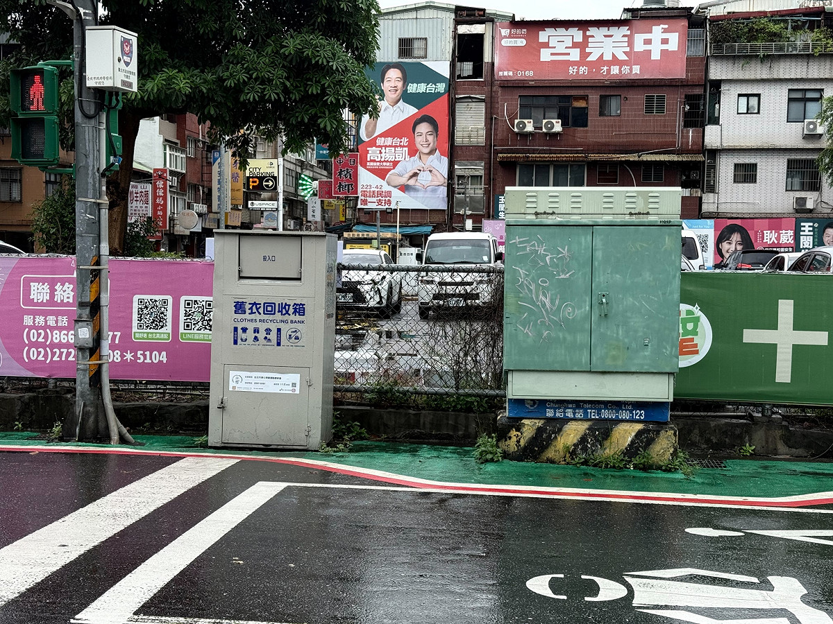 北市標線型人行道在過變電箱時往道路放寬，讓路人繞過箱體前進，接著碰上舊衣回收箱及路燈柱時，卻未比照變電箱繞道，人行道的寬度與路燈底座一樣寬，根本沒行人走路空間。 圖：劉品妡競選團隊 / 提供