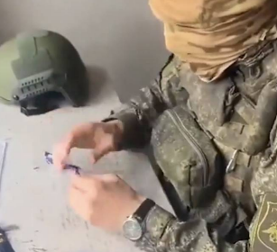 一名俄羅斯軍官在烏克蘭戰區的戰壕掩體內，用美工刀小心翼翼地切開一些在戰場上發現的糖果與巧克力包裝，仔細檢查內部是否被夾帶異物或危險物品。 圖：翻攝自 X @Aisha