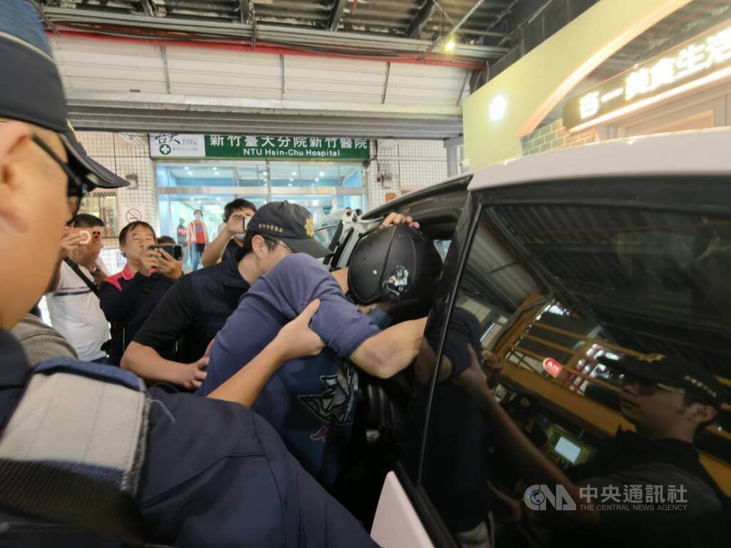 國立陽明交通大學林姓教授（頭戴黑色安全帽者）日前涉嫌在新竹市一處音樂教室，持藍波刀砍殺紀姓連襟店長致死，遭警方開槍制伏後送醫；林男傷勢穩定，24日由警方戒護出院，移送新竹地檢署偵辦。他面對記者詢問全程不發一語，手肘仍有瘀青，需由警方攙扶上車。中央社記者郭宣彣攝　115年7月24日