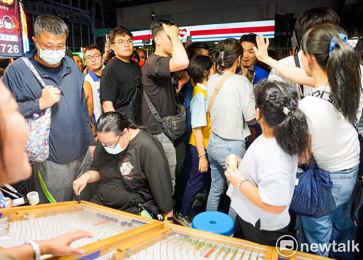 蔣萬安與柯志恩在六合夜市內ㄧ攤ㄧ攤的賣力拜票，一位市民則專注的打彈珠。 圖：張良一/攝