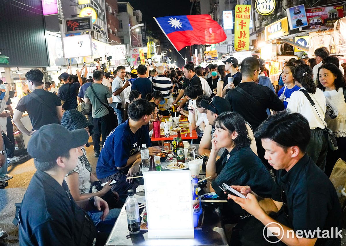 高雄六合夜市的國際觀光客眾多，一些來自日本的觀光客不受選舉掃街激情影響，淡定的坐著等待他們點的美食上桌。 圖：張良一/攝