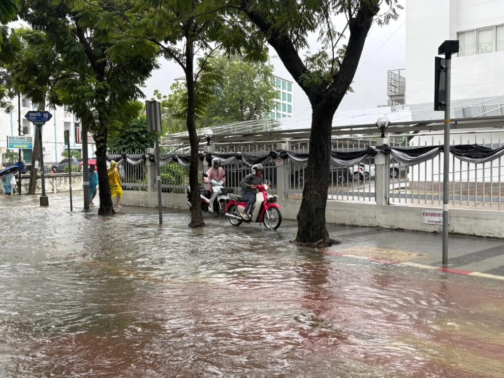 泰國曼谷26日降下大雨，多處道路出現淹水，民眾冒雨涉水通行，機車也受積水影響。（民眾提供）