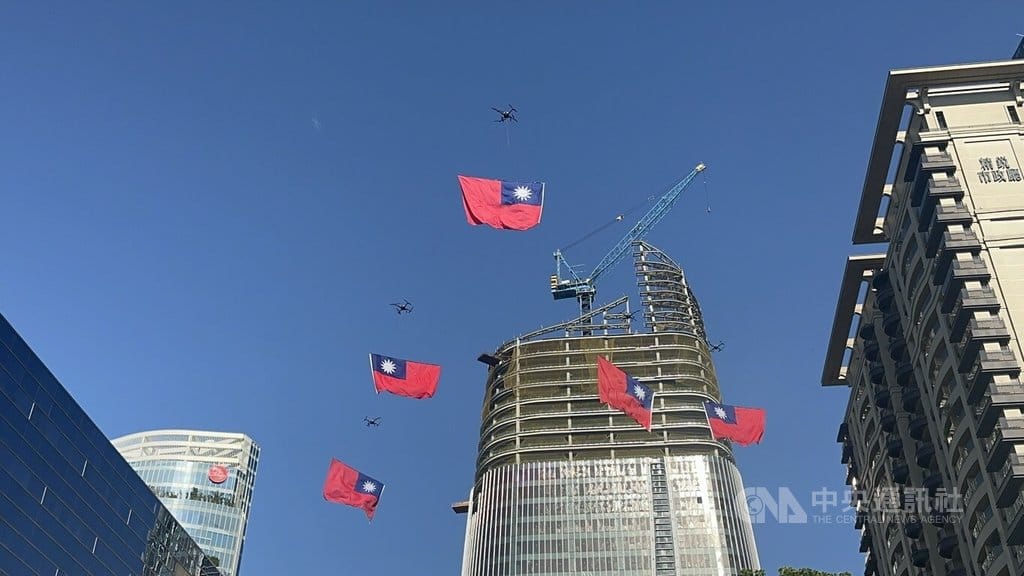 台中市政府10日舉辦國慶升旗典禮，無人機垂掛國旗飛過市府前廣場上空。  圖/中央社