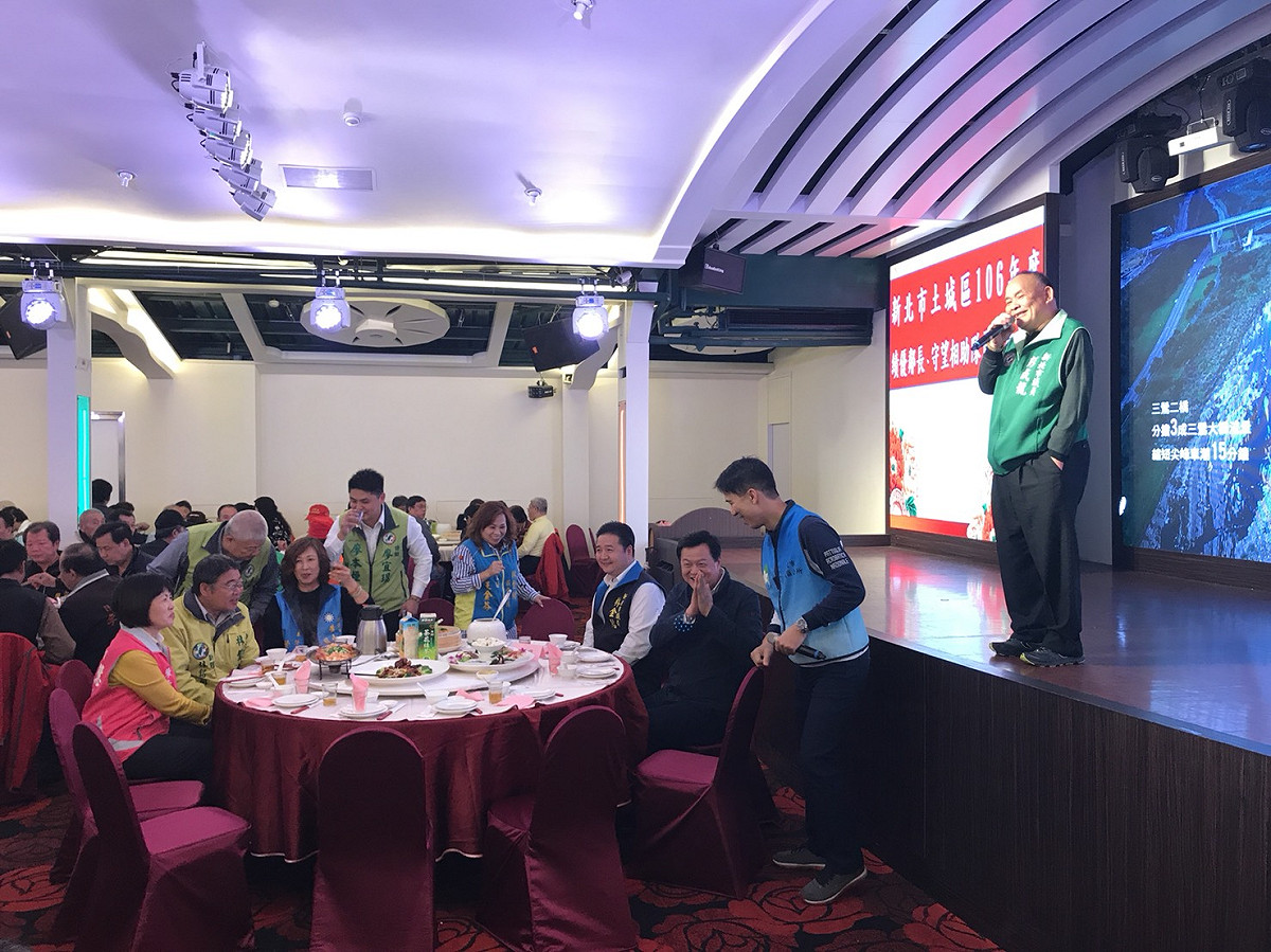 周錫瑋12月1日趕到土城一場基層餐會，議員林金結陪坐在旁，公所的工作人員趨前向周說明無法讓他上台致詞；台上致詞的民進黨議員彭成龍不忘介紹周錫瑋。 圖：讀者/提供