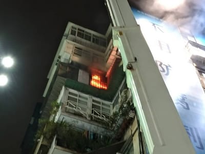 台北市忠孝東路知名百貨旁大樓傳出火警，派出消防人員趕赴現場，屋內橘色火光清晰可見，並飄出陣陣白煙，目前持續搶救中。（民眾提供） 圖：中央社