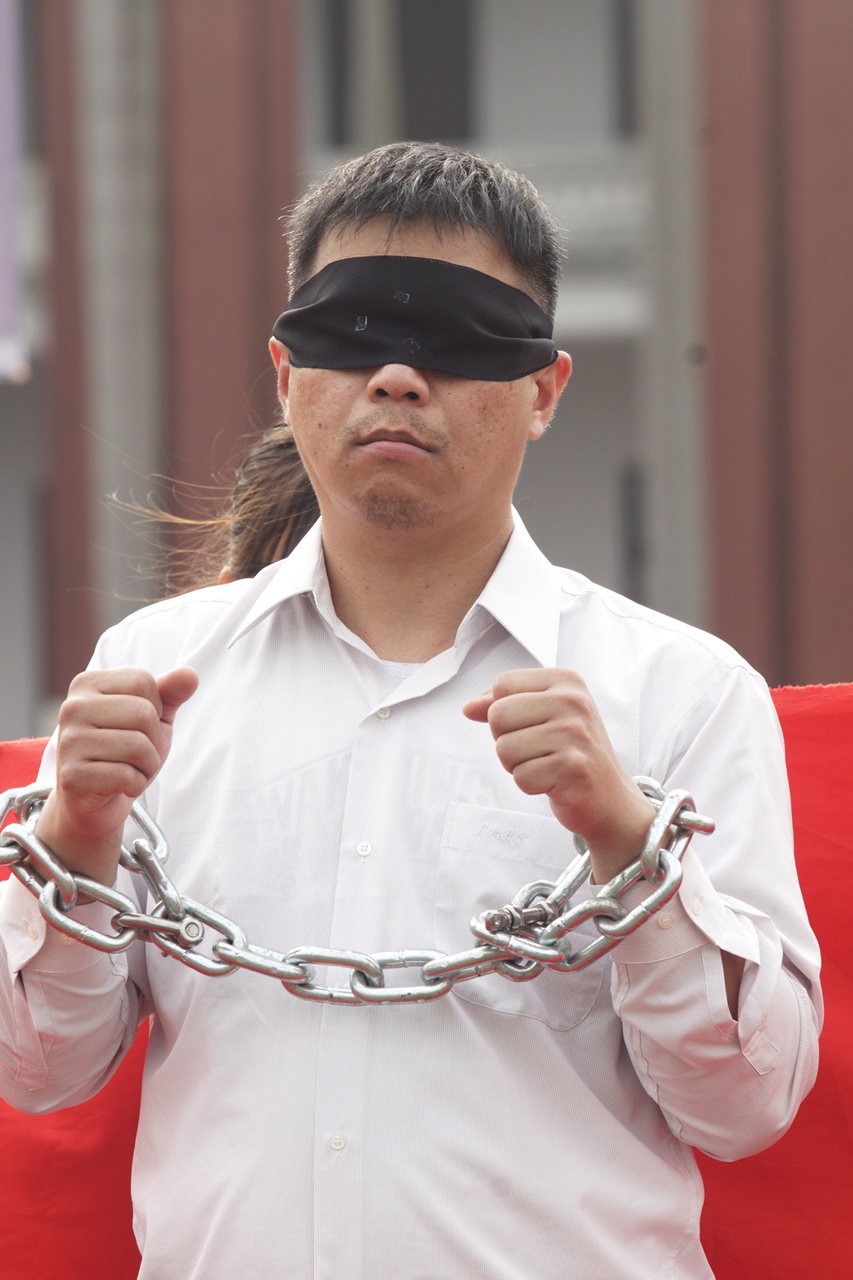 頭帶眼罩、手上鐵鍊象徵李明哲無法與外界溝通。 圖：張良一/攝