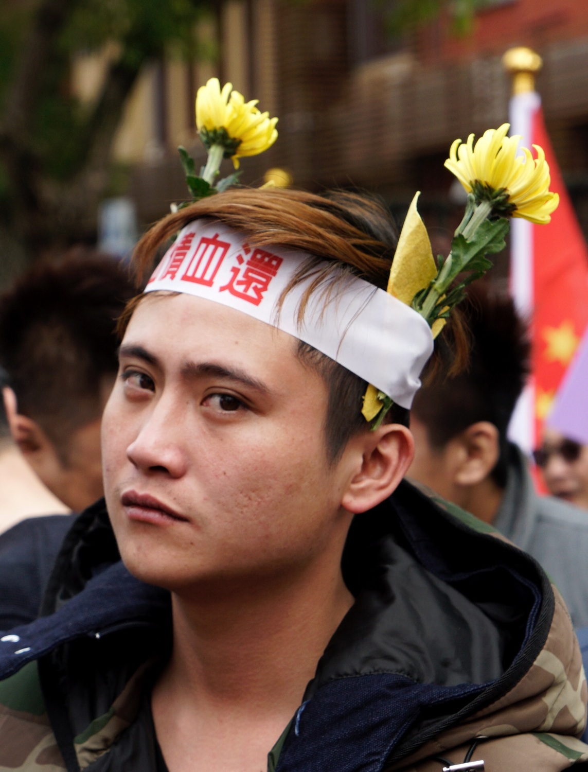 一位統促黨成員頭插兩朵黃菊花，並綁著「血債血還」白布條，他被同伴推出去受訪，生卻羞澀的在鏡頭前喊著「血債血還」口號。 圖：張良一/攝