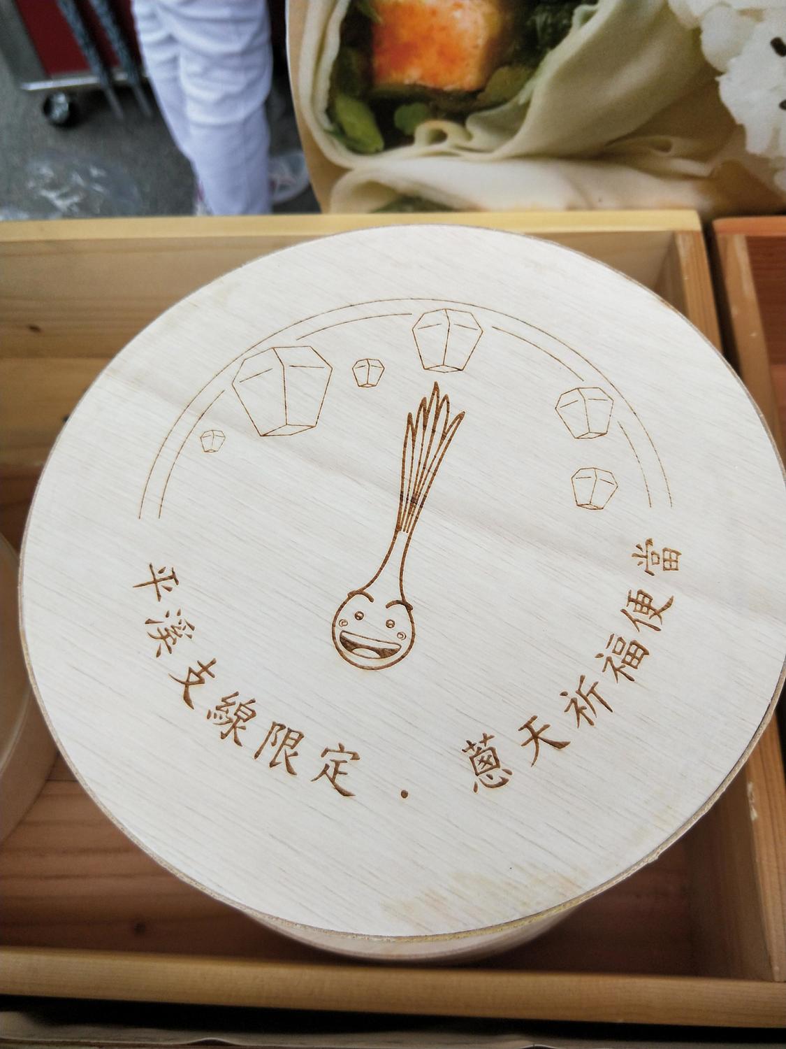 珠蔥便當飯盒則以木製圓形製成，並印有平溪珠蔥的圖樣，外當相當討喜逗趣。 圖：張家綺／攝