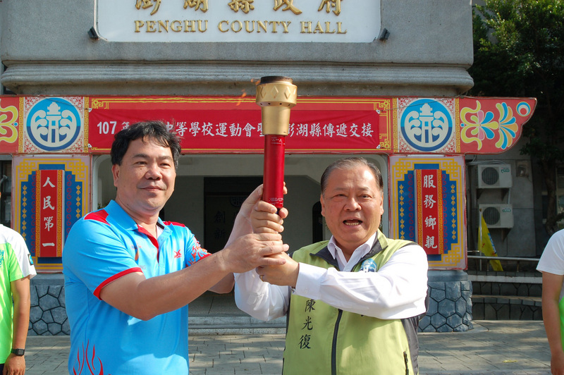 107年全國中等學校運動會聖火16日傳抵澎湖，由台中市南屯區文山國小校長邱炳彰（左）將聖火交接給縣長陳光復（右）後，隨即展開澎湖馬公市區的傳遞。 圖：中央社
