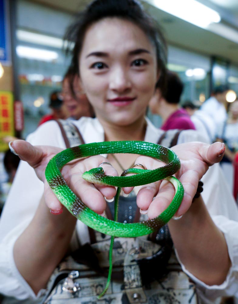 一位女性民眾拿到亞洲蛇肉店的一條綠色仿真蛇回家紀念。 圖：張良一/攝