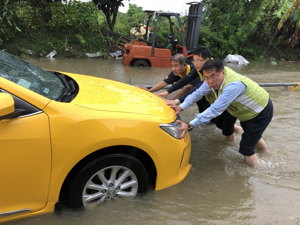 黃偉哲勘災時見一輛計程車因誤入積水區而拋錨，立即捲起褲管，涉水協助司機將計程車推回地勢較高處。 圖：黃偉哲競選總部/提供