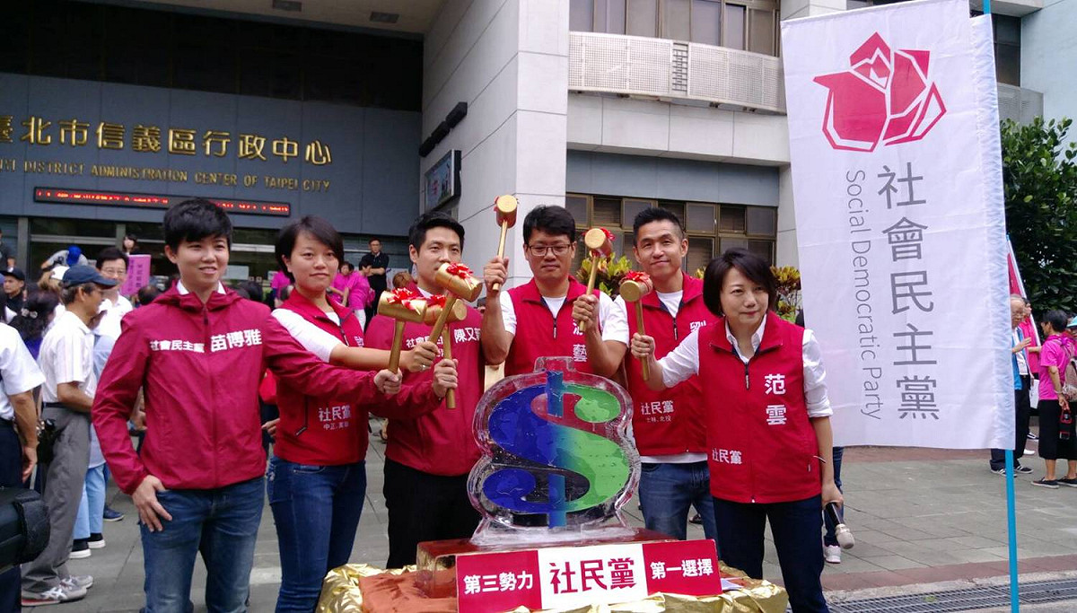 社會民主黨台北市五位市議員候選人高舉鐵鎚，奮力敲碎藍綠色的「$」字冰雕，象徵齊心「打破」藍綠金錢舊政治。 圖：社民黨提供