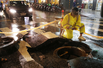 台北市8日大雨造成西門町人孔蓋暴衝，台北市衛生下 水道工程處晚間指出，雨量過大所造成的巨大壓力可能 導致人孔蓋因為「氣衝」或「水衝」而暴衝。圖為衛工 處人員到場處理善後。 圖：中央社