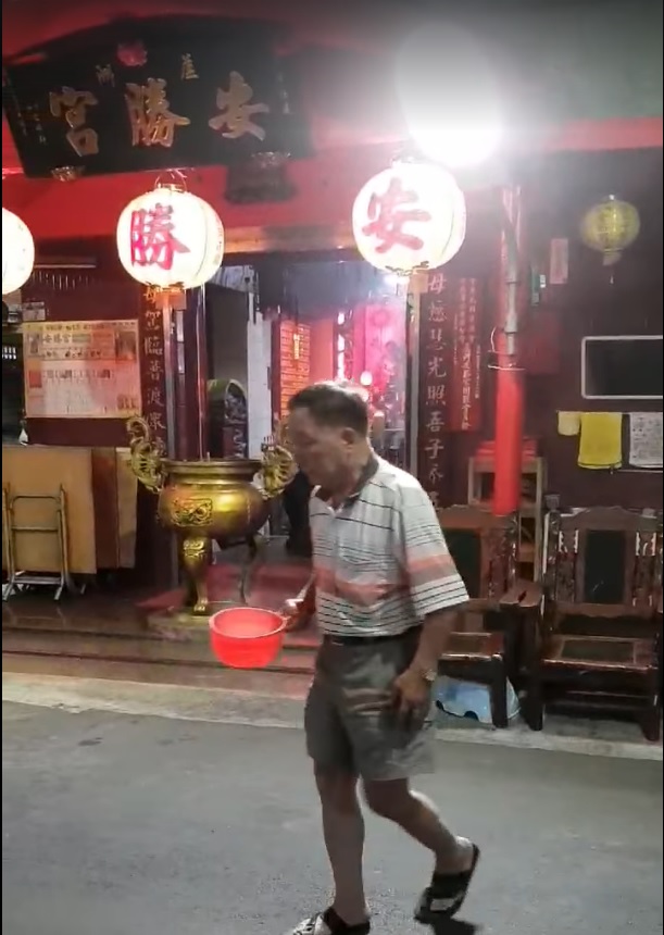 這位疑似虐貓的中年男子，先在宮廟裡裝滿熱水，接著便朝路邊躲在一輛轎車下的流浪貓走去。 圖：翻攝自臉書社團《貓咪也瘋狂俱樂部 CrazyCat club》