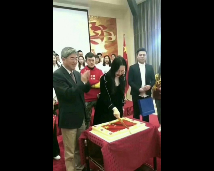 一名站在中國駐保加利亞大使張海舟身旁的女子手持長刀，從中間切開五星紅旗圖案的蛋糕，張海舟則在一旁微笑鼓掌。 圖：翻攝自Youtube