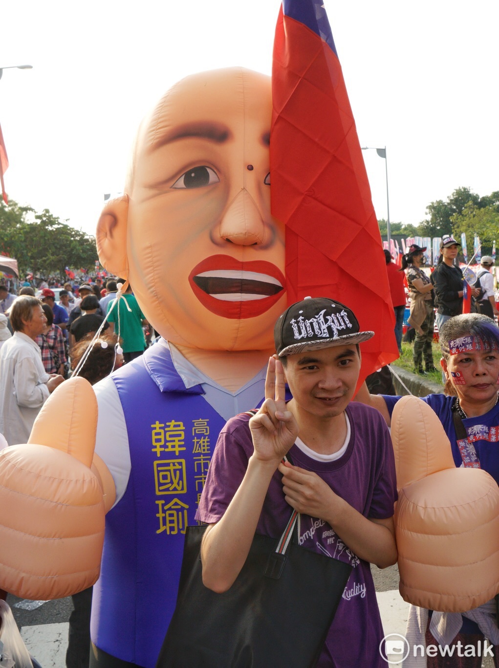 一位民眾在韓國瑜充氣人像前比出勝利手勢，有趣的是這同時也是陳其邁號次的手勢。 圖：張良一／攝