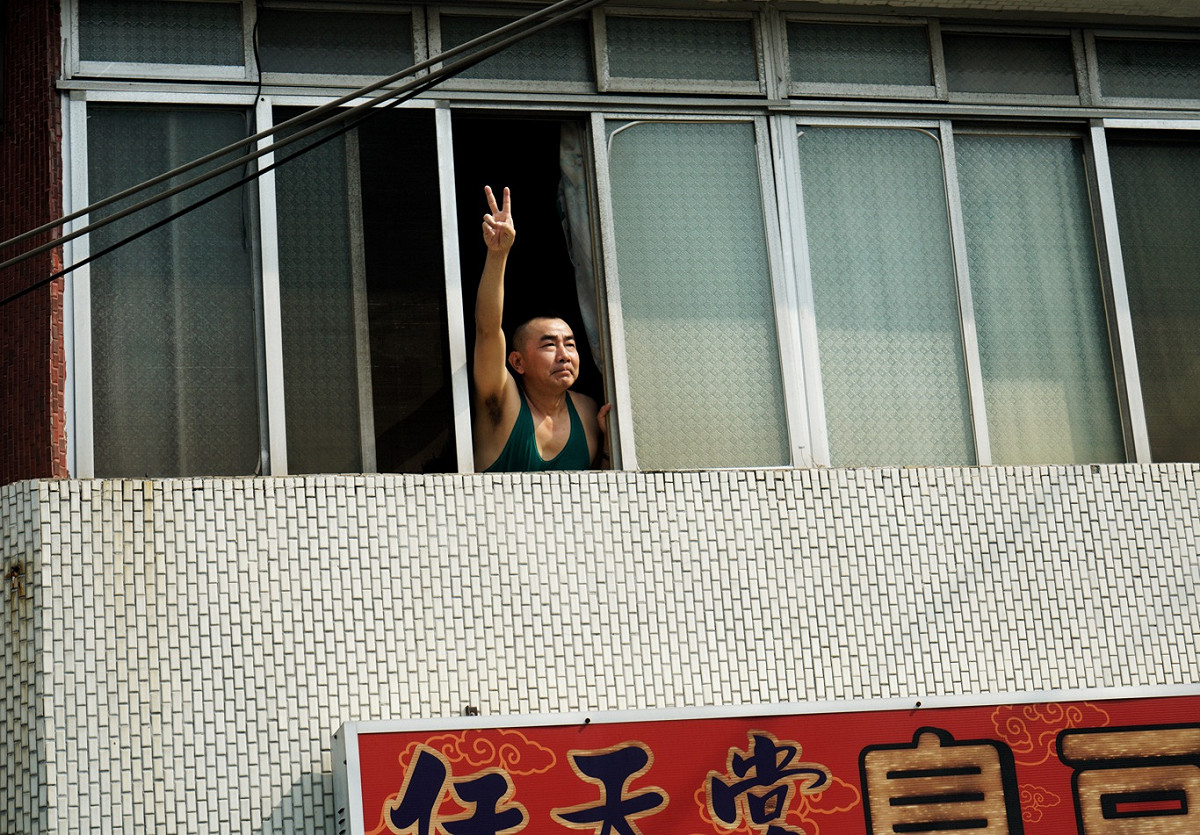 一位民眾在自家二樓窗口高舉著陳其邁競選號次的手勢。 圖：張良一/攝