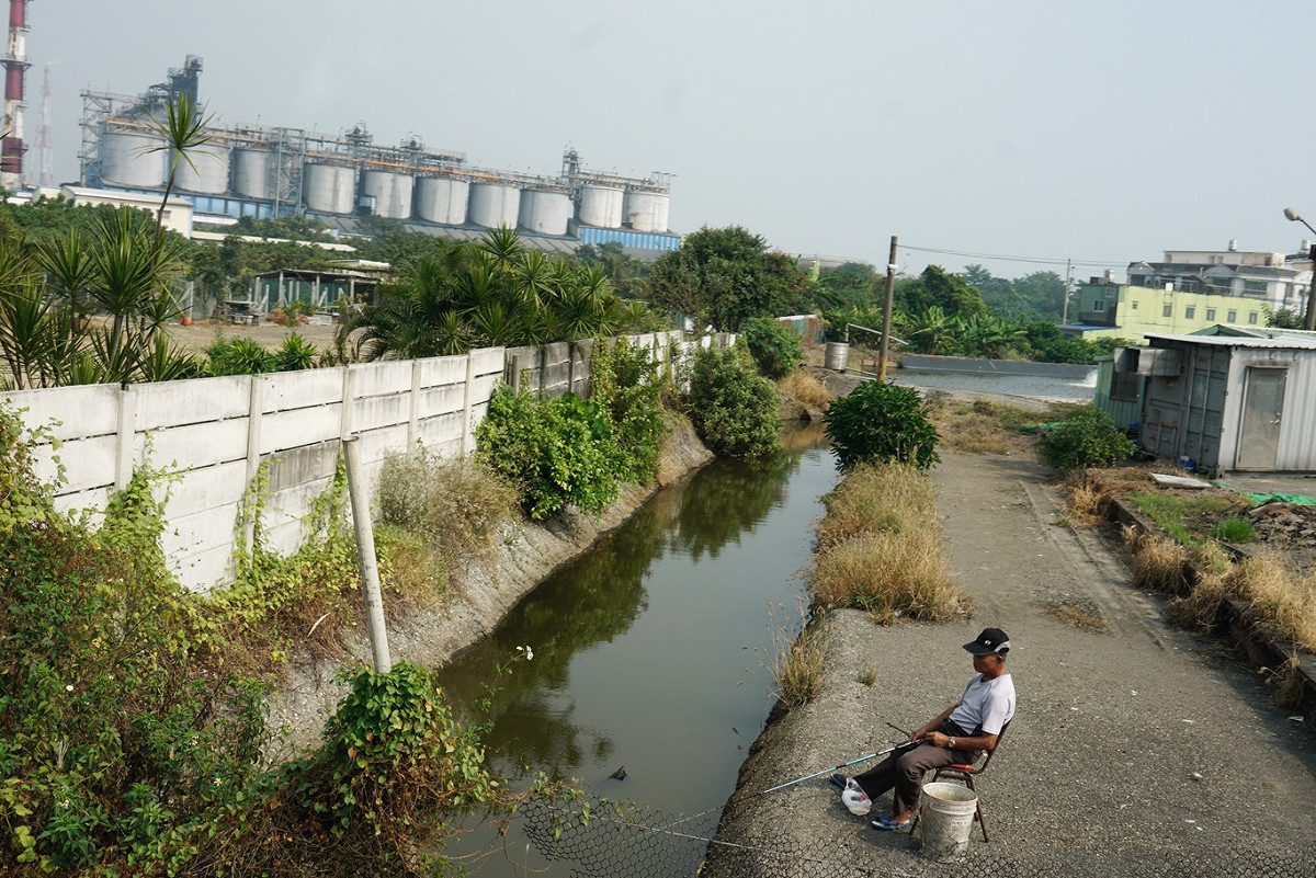 一位民眾在林園石化園區外的水圳釣魚，絲毫不被陳其邁競選車隊的啦叭聲影響。 圖：張良一/攝
