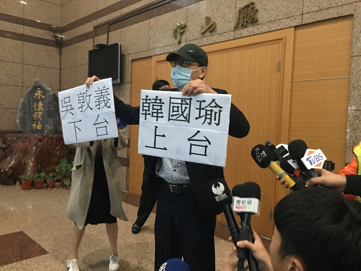 中常會召開前，有民眾手持「吳敦義下台、韓國瑜上台」告示牌抗議。 圖：趙婉淳／攝