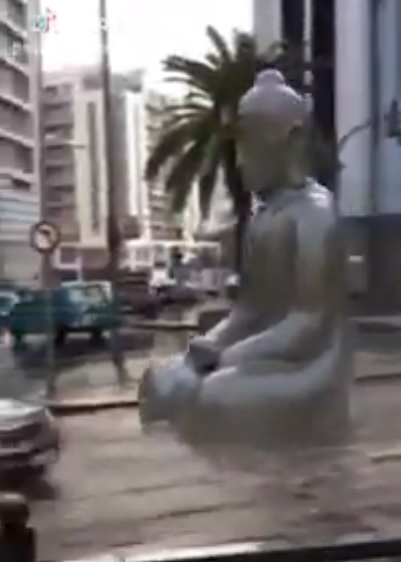 從影片中可以看出，一尊巨大佛像從高處街道緩緩順著水流漂向大馬路，旁邊還有車輛在行駛。 圖：翻攝自Youtube