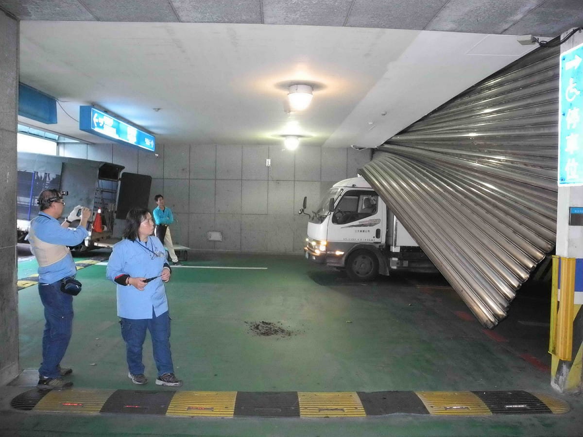 新北市府地下停車場B2到B1的西側入口處大型鐵捲門突然墜落，市府員工及機電人員在現場查看。  圖：王峻昌/攝