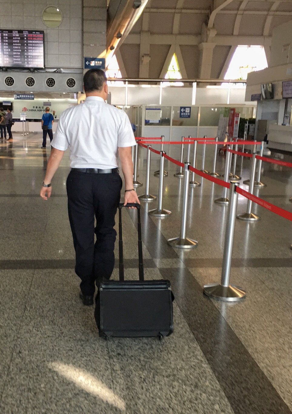一位沒有參與罷工的華航機師拉著行李箱走進高雄小港國際機場出境大廳時，經過空蕩蕩的華航報到櫃檯，準備執勤。 圖：張良一攝