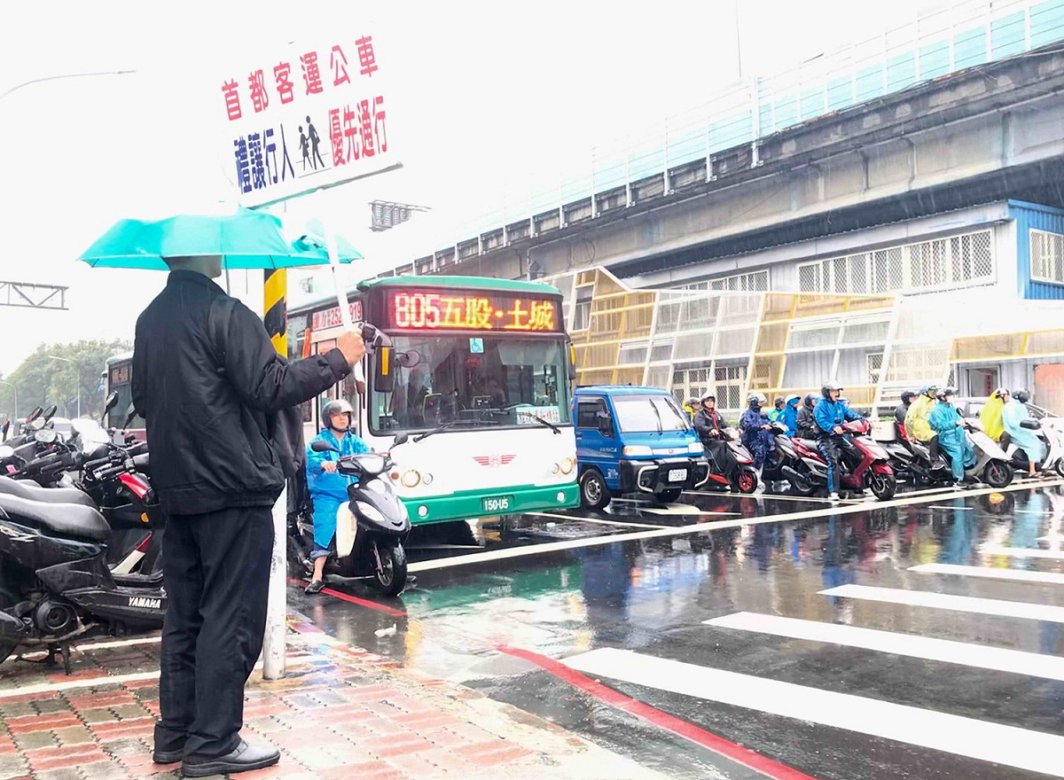 首都客運派員在路口的停等區，舉牌向公車駕駛宣導「禮讓行人」。 圖：新北市交通局提供