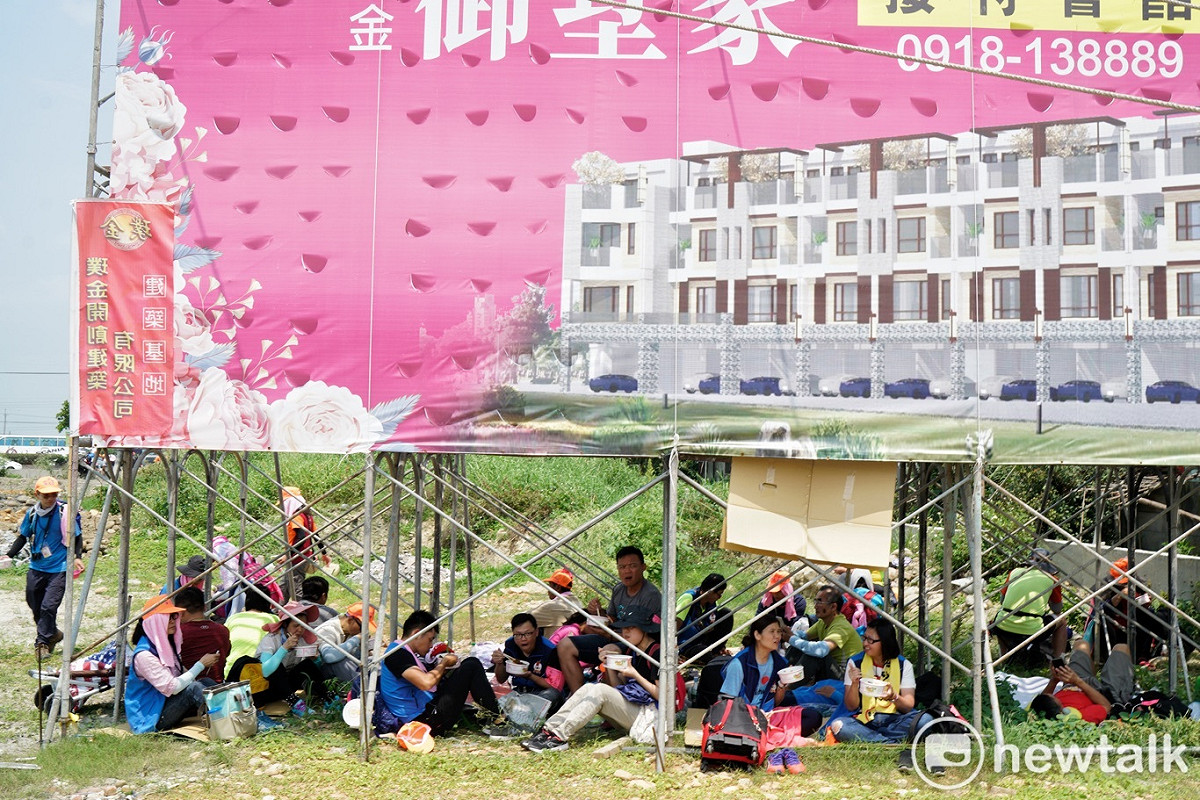正中午天氣炎熱，而且太陽又大，許多信眾或蹲或坐，在廣告鷹架下方躲太陽。 圖：張良一/攝
