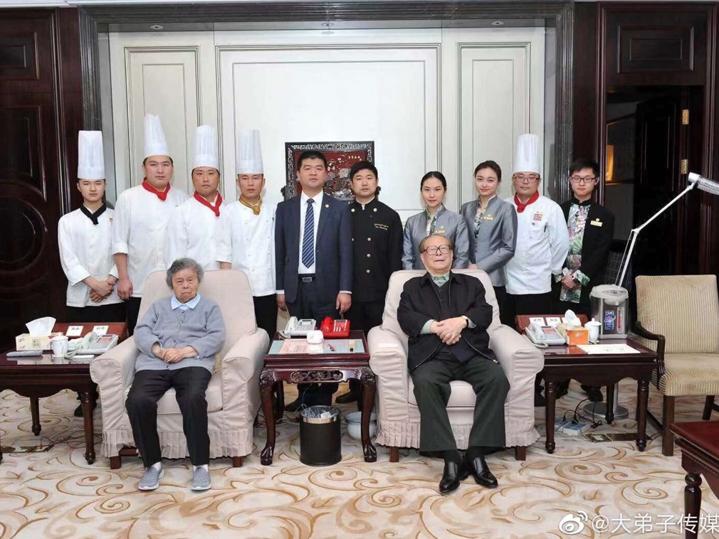 照片顯示，江澤民（前排右）和夫人王冶坪靠坐在沙發上，江澤民內襯橄欖綠衣服，雙手抱著置於腹前。江澤民和王冶坪身後站著酒店十位工作人員。 圖：翻攝自大弟子傳媒Leo微博帳號
