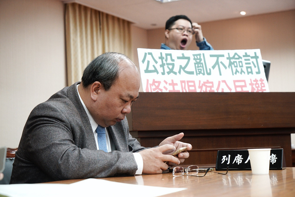 中選會主委陳朝建枯坐滑手機。 圖：張良一/攝