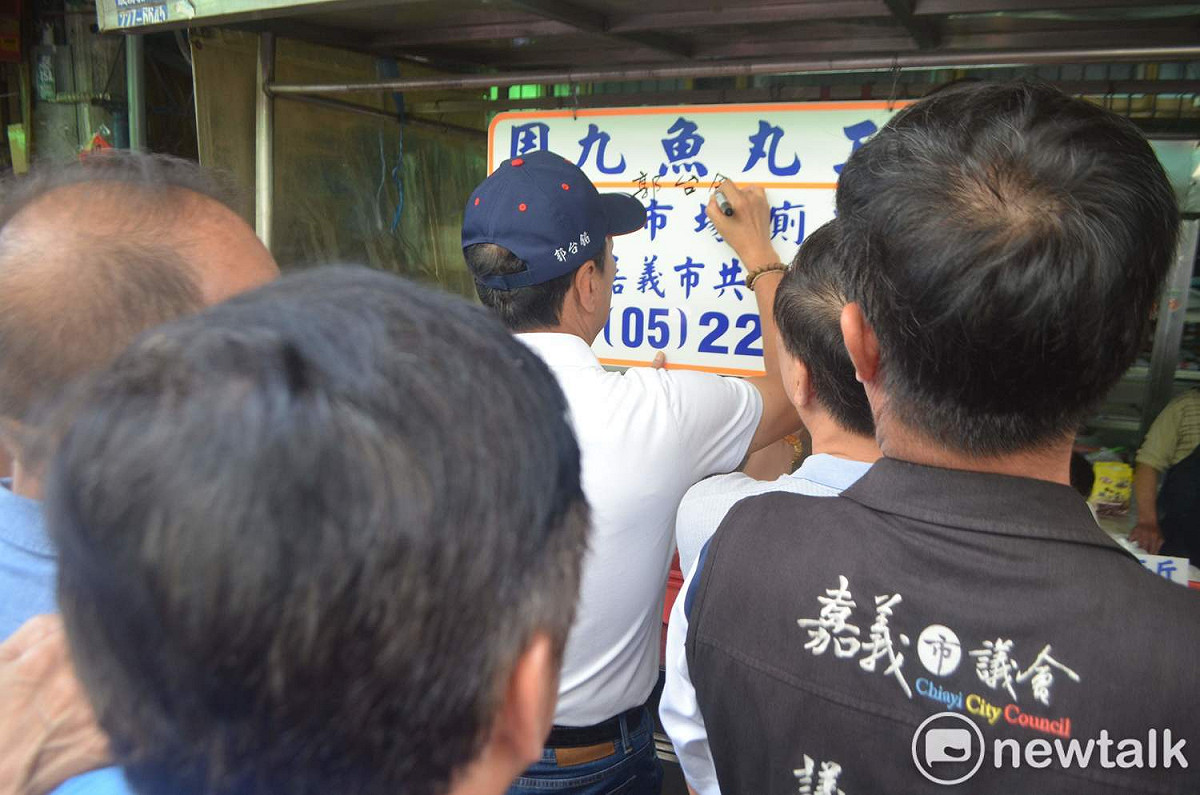 郭台銘今天造訪嘉義東市場，應邀在攤商的廣告看板上簽名，體會「馬英九」級的禮遇。 圖：蔡坤龍/攝