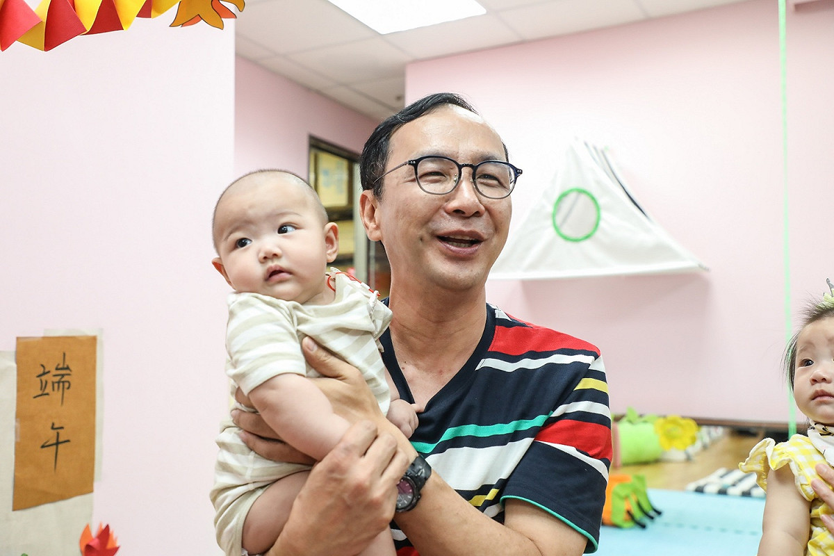 朱立倫參訪土城托育中心，重新回味奶爸生活，幫小嬰兒按摩、餵飯，還當起孩子的大玩偶，陪小朋友溜滑梯、玩遊戲。 圖：朱立倫辦公室／提供