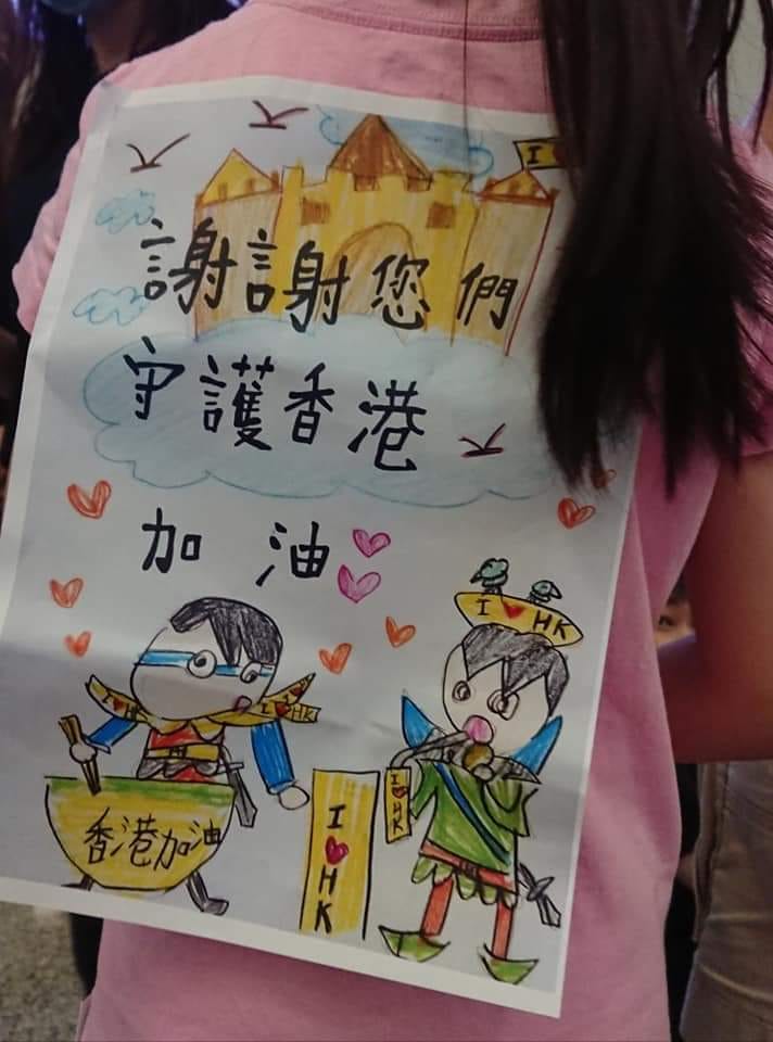 有網友在王丹臉書底下留言，指出當天在機場，還有一名小女孩與兩個小男生，發餅乾給現場留守的市民，背上同樣背著標語，寫著「謝謝您們守護香港」 圖：翻攝自王丹网站  Wang Dan's Page
