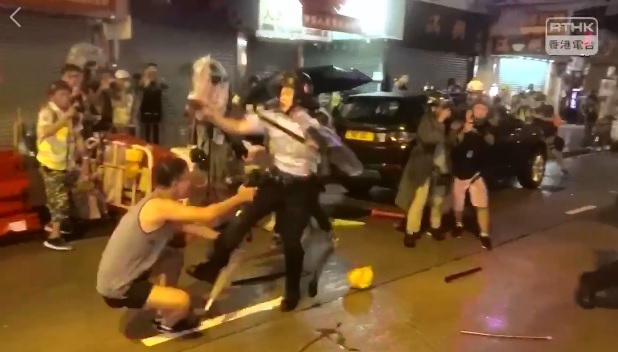 香港警察在荃葵青大遊行警民衝突中拔出左輪手槍，1名男子（左）跪求員警別開槍，卻被一腳踢開。 圖：翻攝自香港電台視像新聞 RTHK VNEWS影片