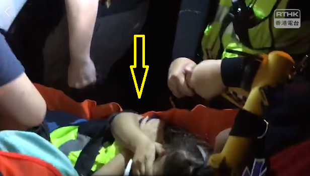香港旺角8日晚間警民衝突升級，警方開槍強勢清場時，1名女急救員（箭頭處）腳部中彈，被抬上擔架送醫。 圖：翻攝自香港電台視像新聞臉書影片